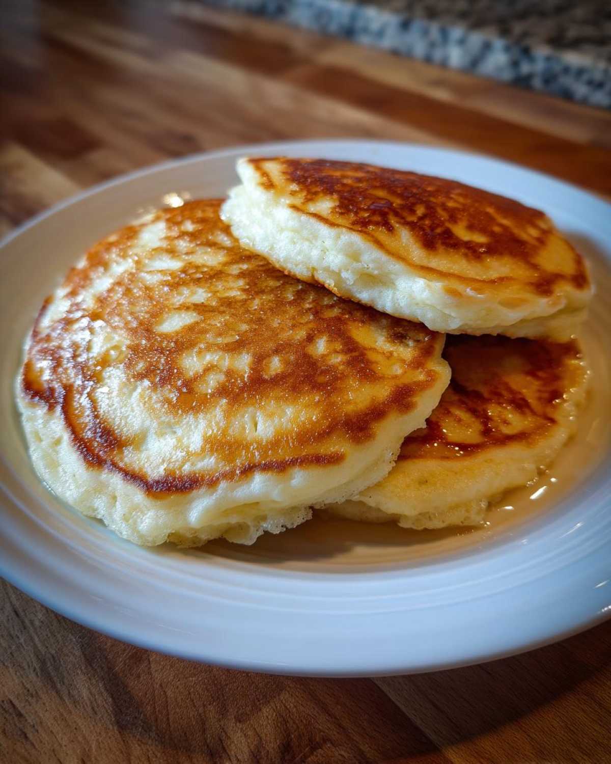A stack of three thick, fluffy greek yogurt pancakes with golden brown tops sitting on a white plate.
