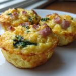 Three fluffy muffin tin egg bites topped with ham and spinach served on a white plate.
