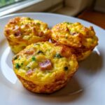 Three fluffy muffin tin egg bites with visible chunks of ham and green herbs on a white plate.