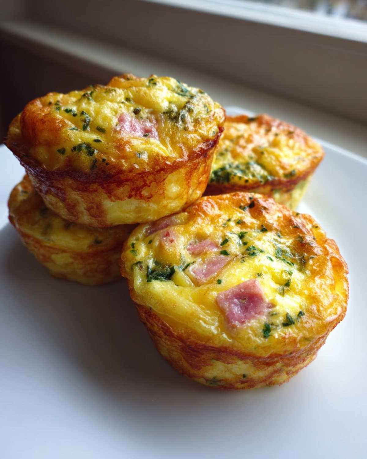 A stack of four fluffy muffin tin egg bites featuring visible pieces of ham and green herbs.