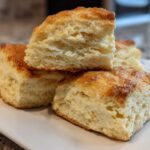 Close-up of fluffy, square-cut scones stacked on a white plate, showing their layered interior texture.