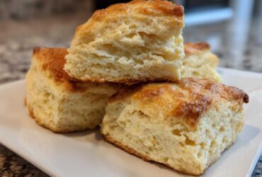 Close-up of fluffy, square-cut scones stacked on a white plate, showing their layered interior texture.