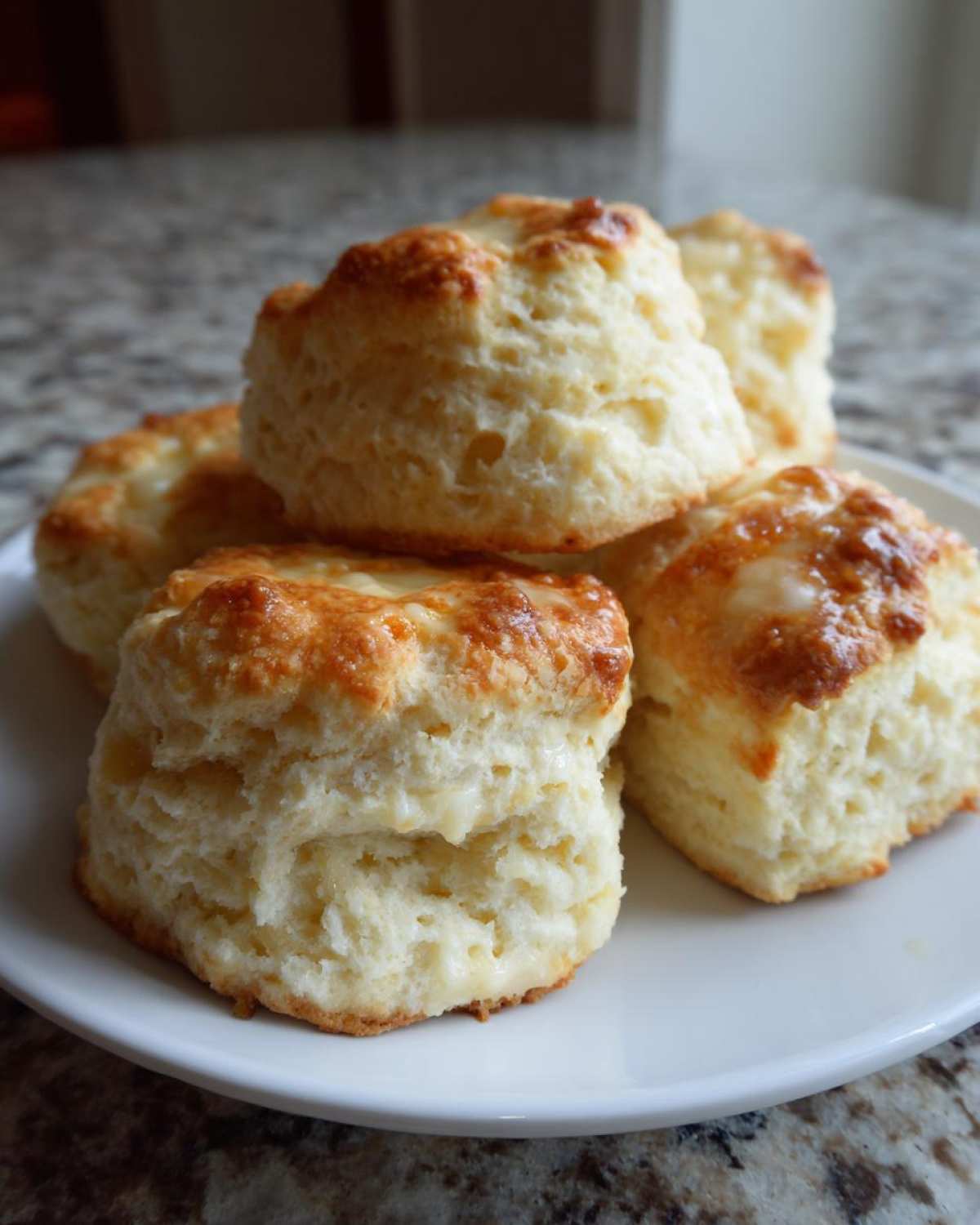 A stack of five golden-brown, fluffy homemade scones resting on a white plate.