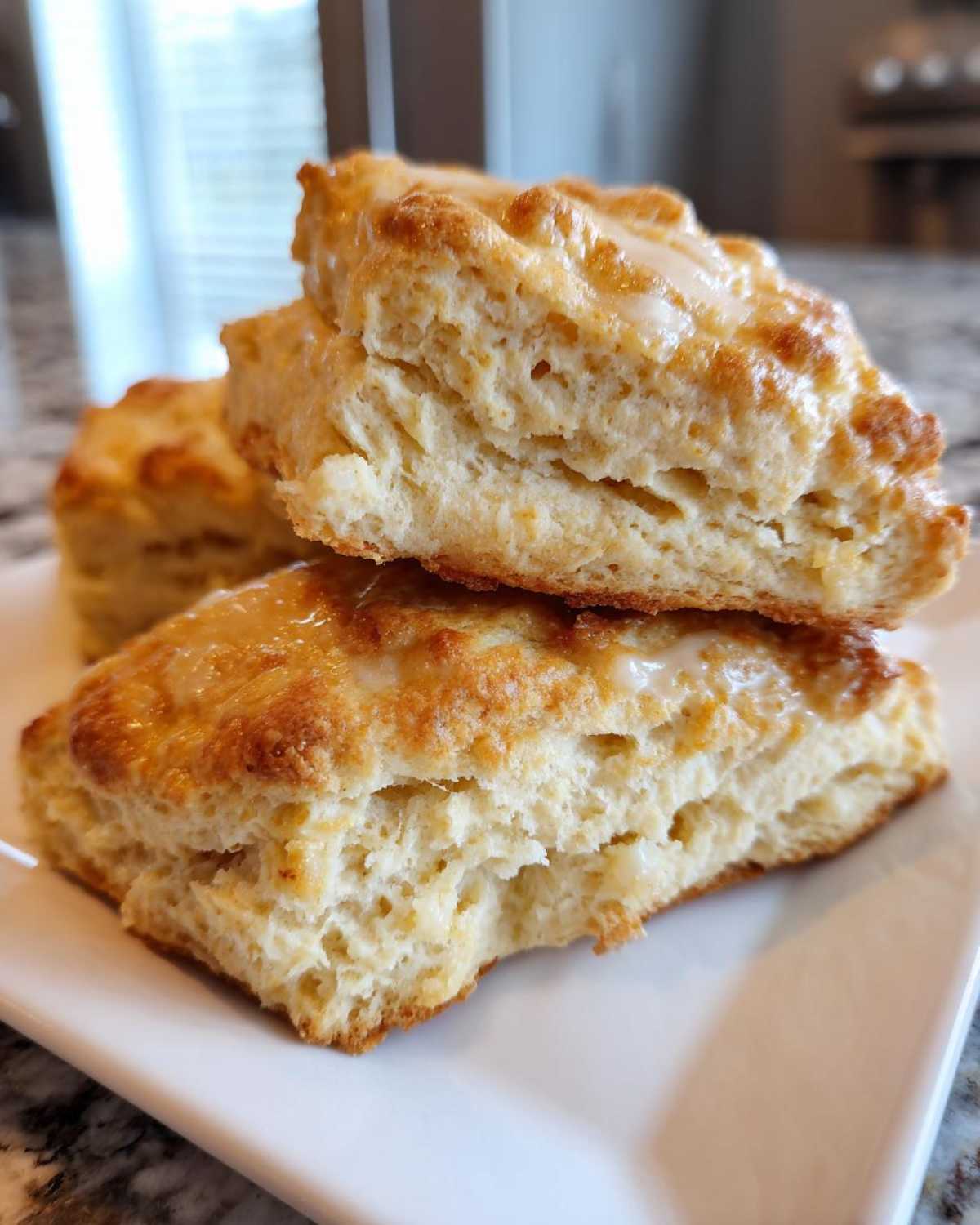 Close-up of fluffy, layered scones stacked on a white plate, topped with a light glaze.