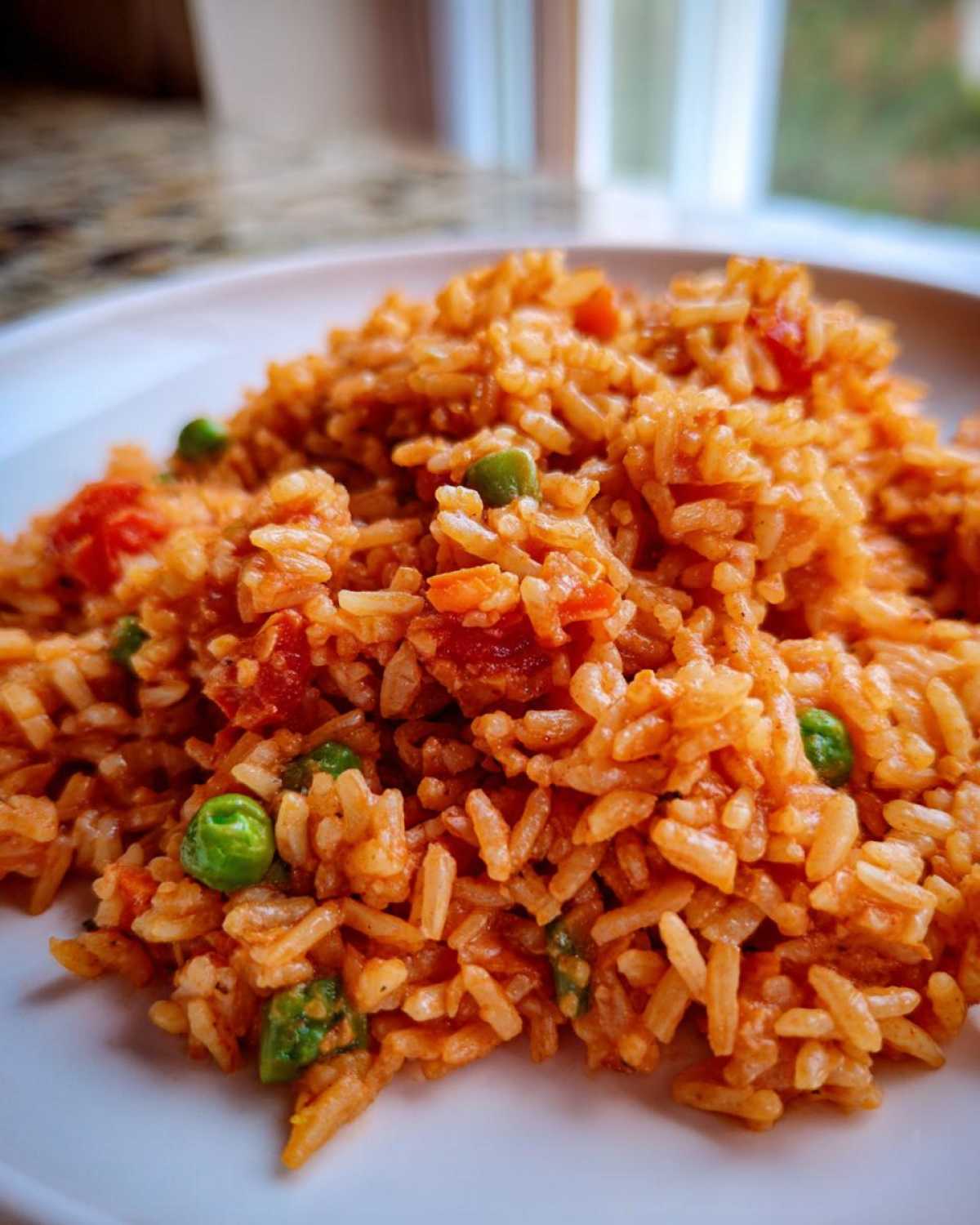 Close-up of fluffy, orange-red spanish rice mixed with bright green peas and diced tomatoes on a white plate.