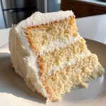 Close-up of a moist slice of vanilla cake recipe showing two layers and thick white frosting.