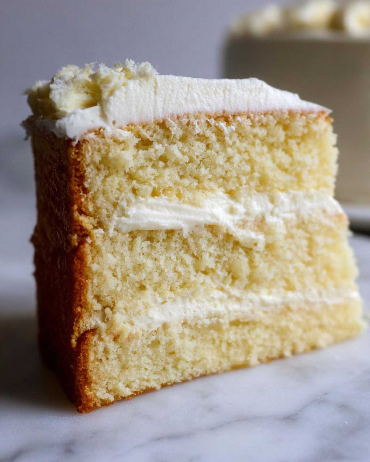 Close-up of a moist slice of vanilla cake recipe showing fluffy layers and white buttercream frosting.