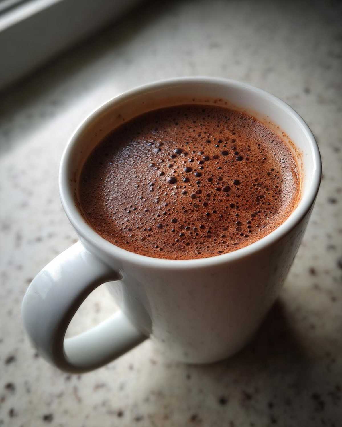 Close-up of rich, foamy homemade hot cocoa in a white ceramic mug.