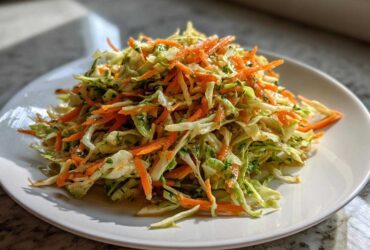 A mound of bright, shredded cabbage salad mixed with julienned carrots and herbs, served on a white plate.