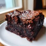 Close-up of a rich, fudgy black bean brownies square topped with melted chocolate chips and flaky sea salt.