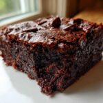 Close-up of a rich, dark, fudgy slice of black bean brownies topped with melted chocolate chips.