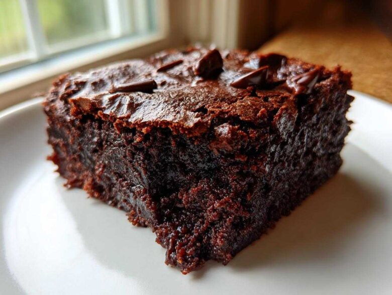 Close-up of a rich, dark, fudgy slice of black bean brownies topped with melted chocolate chips.