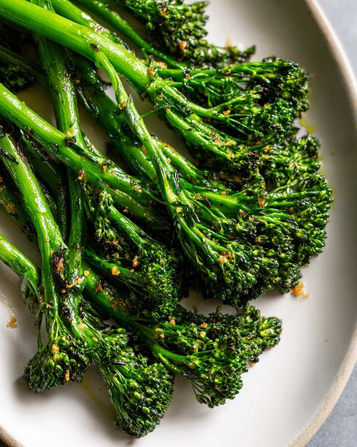 Close-up of bright green, tender-crisp broccolini seasoned with garlic and lemon, served on a light plate.
