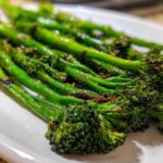 Close-up of vibrant green, charred garlic lemon broccolini spears served on a white dish.