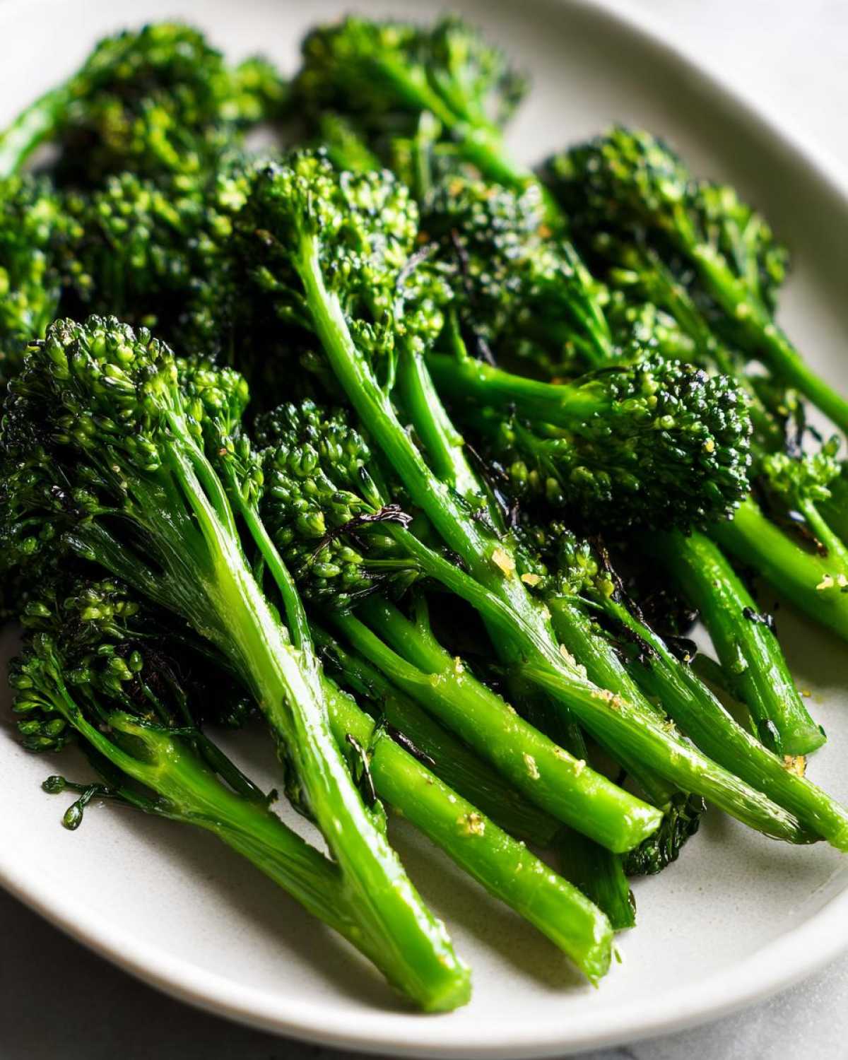 Close-up of vibrant, tender-crisp broccolini stalks seasoned with garlic and lemon, served on a light-colored platter.