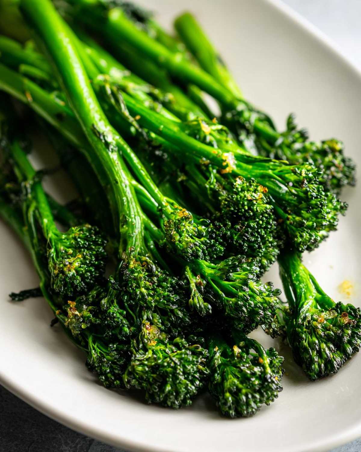 Close-up shot of bright green, perfectly cooked broccolini seasoned with garlic and lemon zest.
