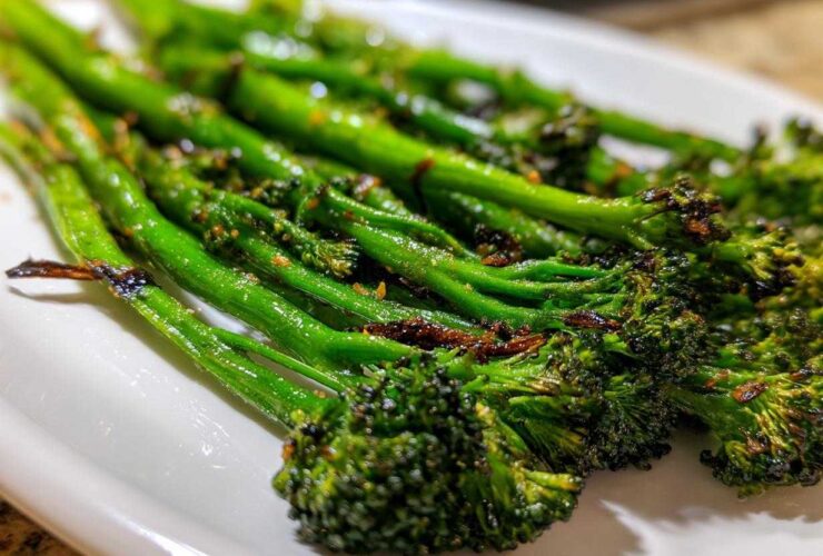 Close-up of vibrant green, charred garlic lemon broccolini spears served on a white dish.