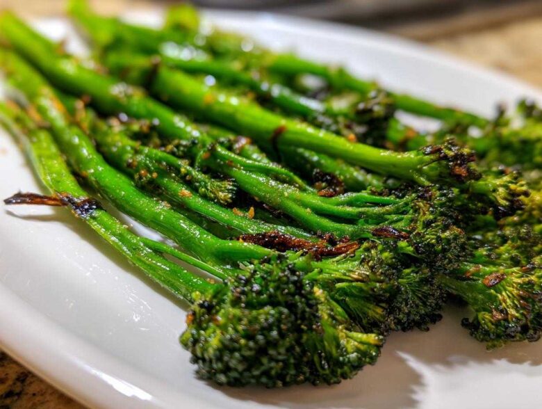 Close-up of vibrant green, charred garlic lemon broccolini spears served on a white dish.
