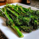 Close-up of bright green, perfectly cooked garlic lemon broccolini served on a white rectangular plate.