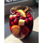 A glass filled with rich red christmas sangria, garnished with cranberries, orange slices, apple cubes, and cinnamon sticks.