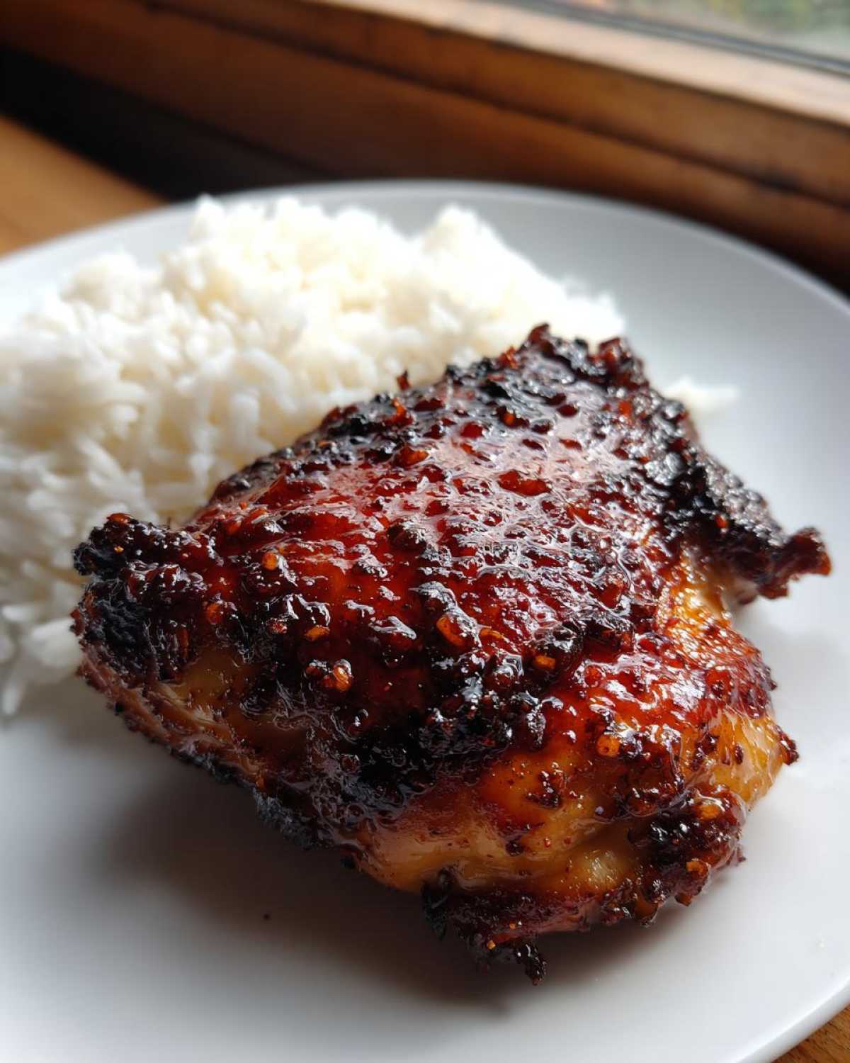 Close-up of a piece of glazed harissa chicken thigh served next to fluffy white rice on a white plate.