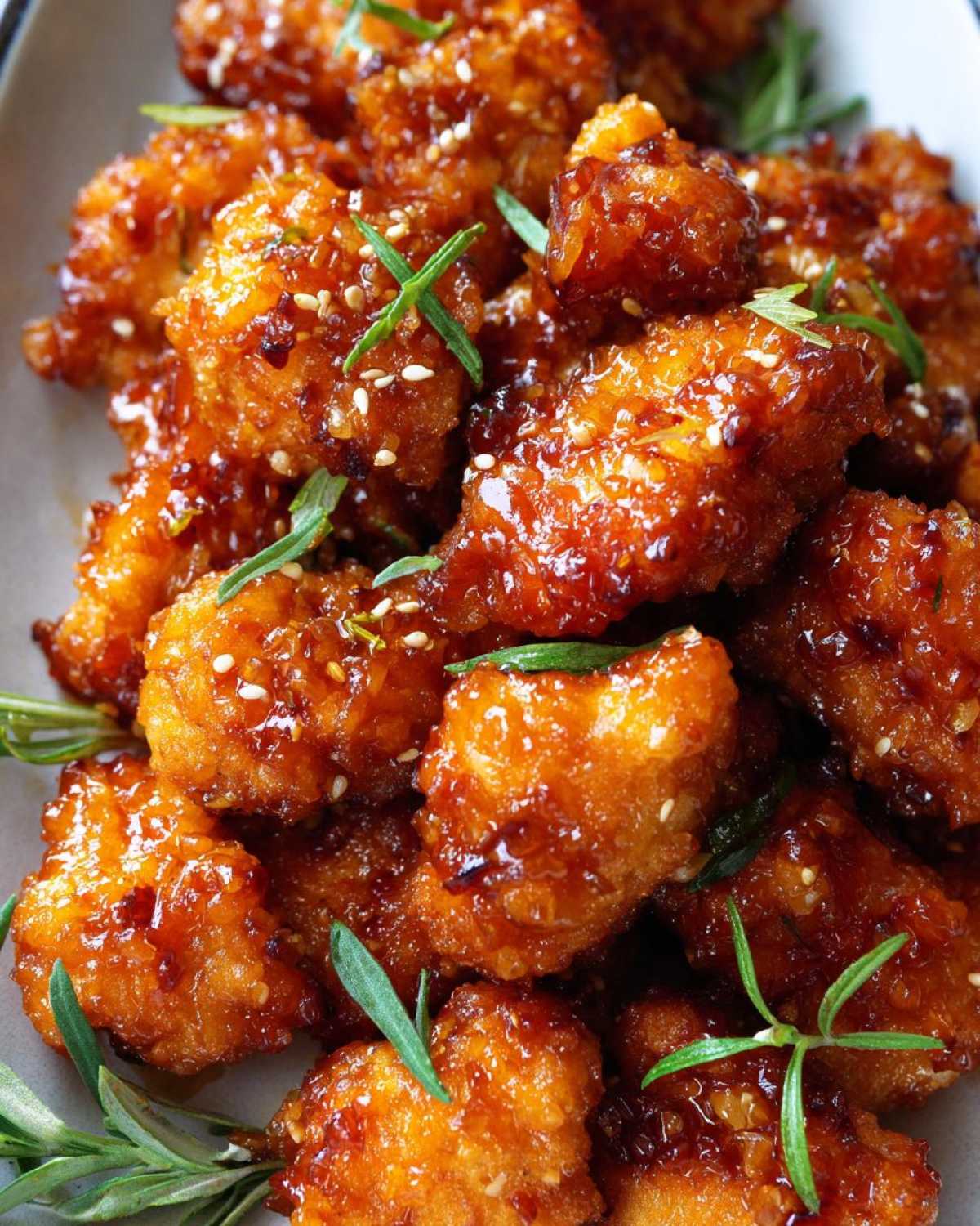 Close-up of crispy, glazed orange chicken recipe pieces garnished with sesame seeds and fresh rosemary sprigs.