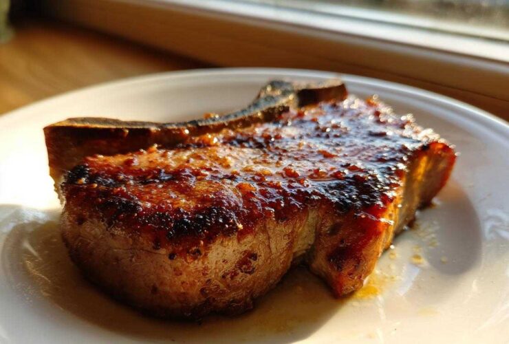 A thick, bone-in pork chop, glistening with a dark glaze, resting on a white plate.