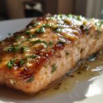Close-up of a perfectly cooked salmon fillet covered in a shiny glaze, garlic, and fresh parsley.