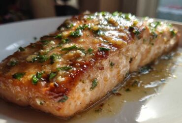 Close-up of a perfectly cooked salmon fillet covered in a shiny glaze, garlic, and fresh parsley.