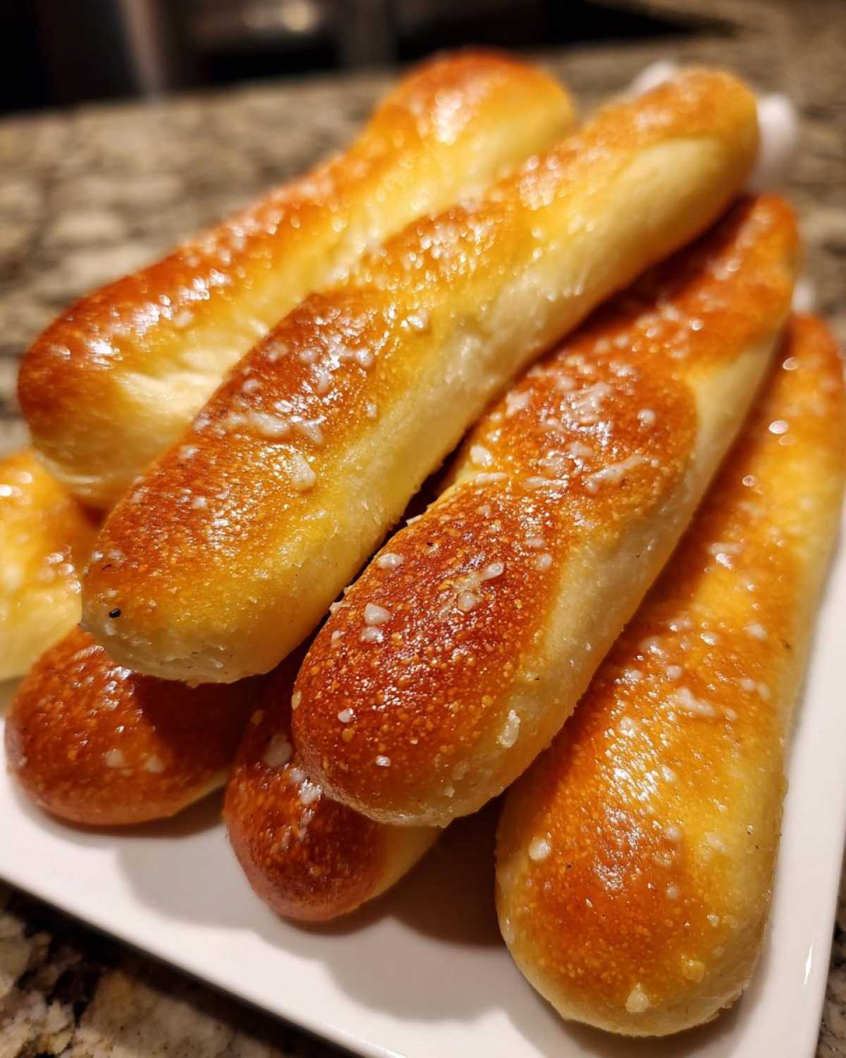 A close-up stack of freshly baked, golden brown breadsticks sprinkled with coarse salt.