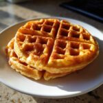 A stack of golden brown, freshly made high protein waffles resting on a white plate.