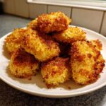 A close-up shot of a pile of crispy, golden homemade chicken nuggets on a white plate.