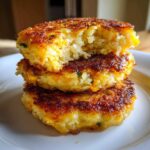 A stack of three perfectly golden brown mashed potato cakes, with a bite taken out of the top one showing the fluffy interior.