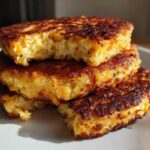 A stack of three golden brown, crispy mashed potato cakes with a fluffy interior, one having a bite taken out.
