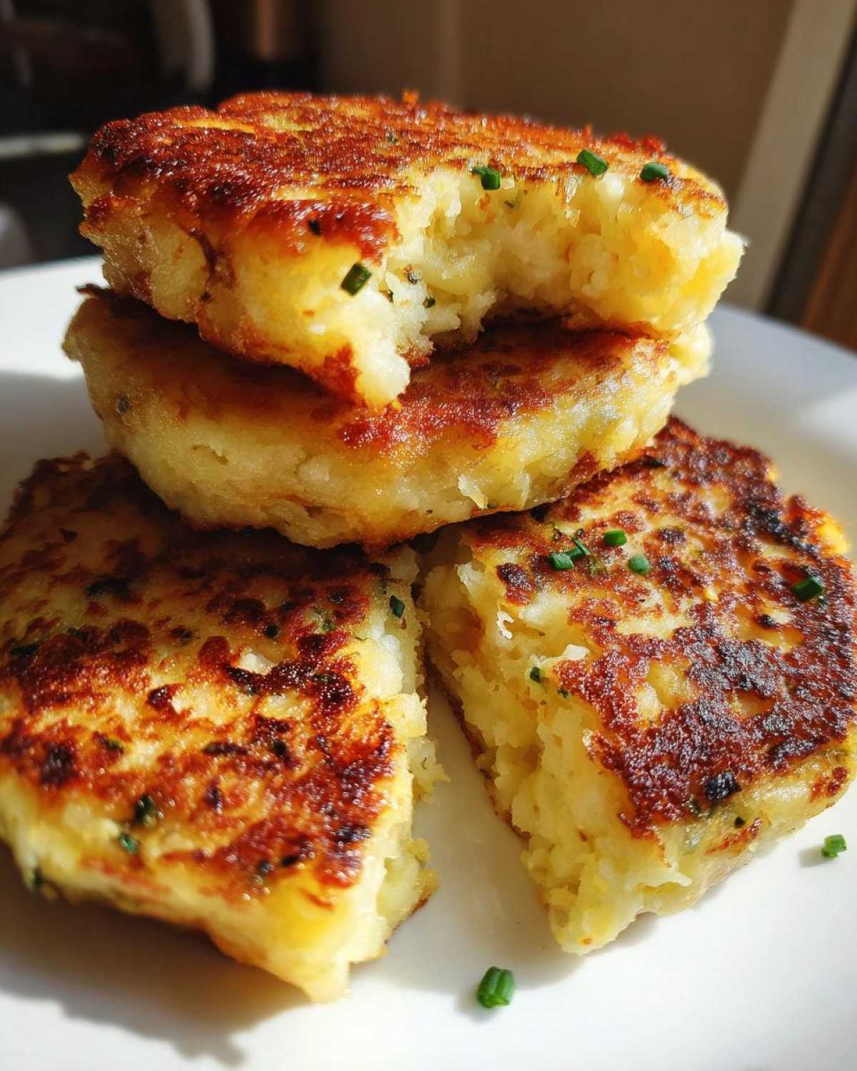 Close-up of golden brown, pan-fried mashed potato cakes stacked, with one cake broken open to show the fluffy interior.