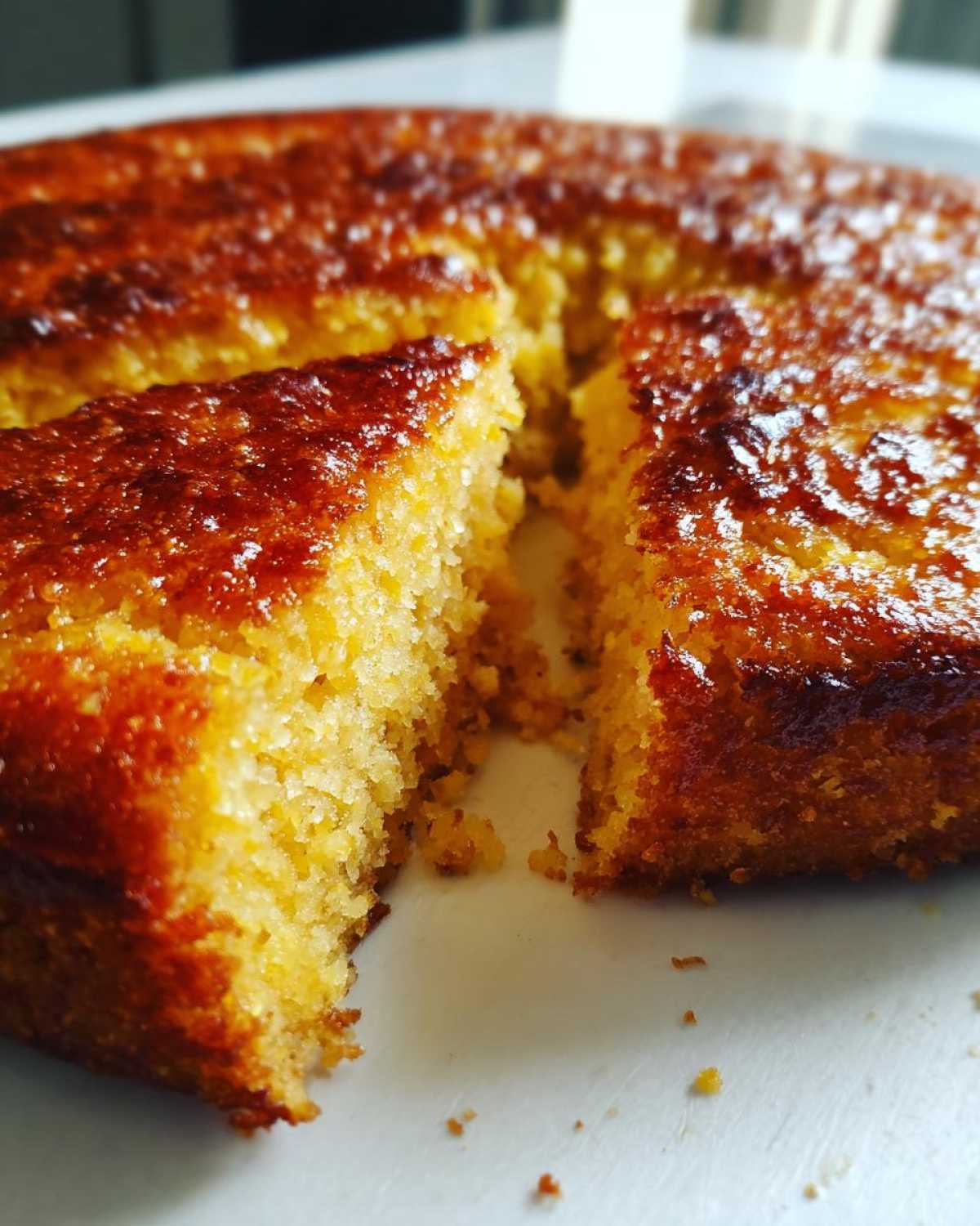 Close-up of a golden, moist slice being pulled from a round skillet cornbread showing its caramelized, crunchy crust.