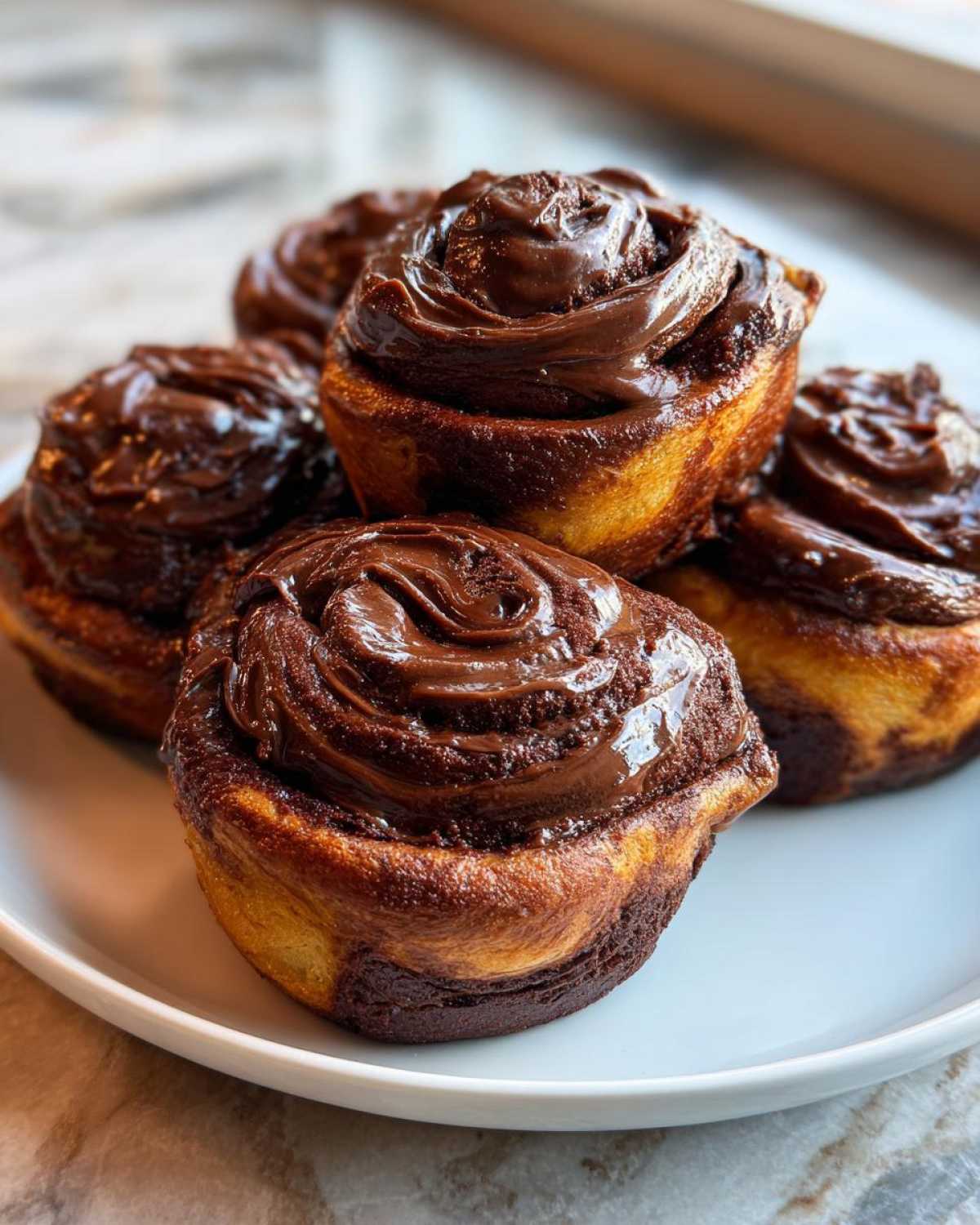 A close-up of several rich, gooey chocolate cinnamon rolls stacked on a white plate.