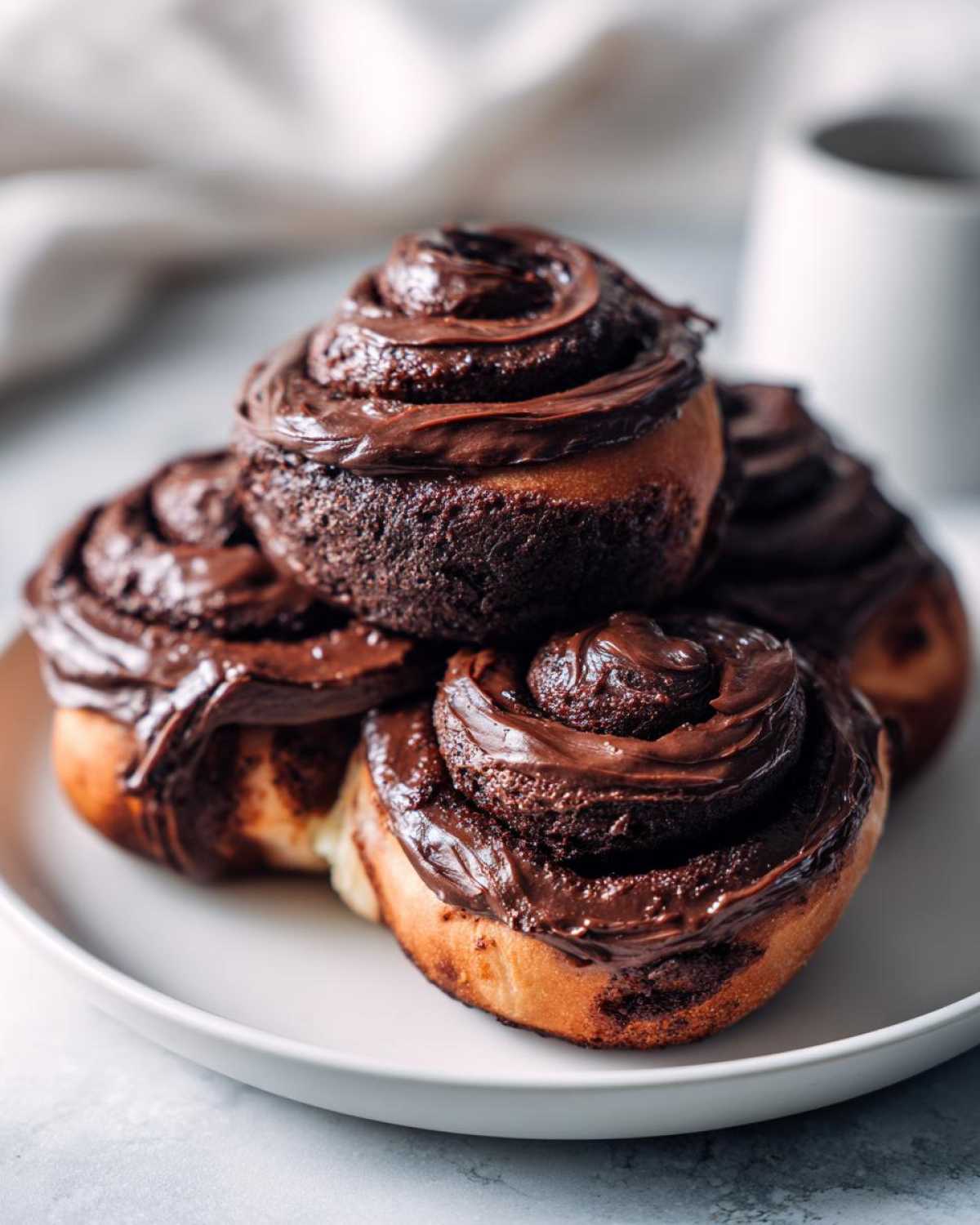 A stack of four rich chocolate cinnamon rolls generously topped with thick, glossy chocolate frosting.