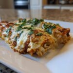 Close-up of two cheesy green chile chicken enchiladas topped with fresh cilantro on a white plate.