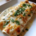 Close-up of creamy green chile chicken enchiladas topped with melted, slightly browned cheese and fresh cilantro.