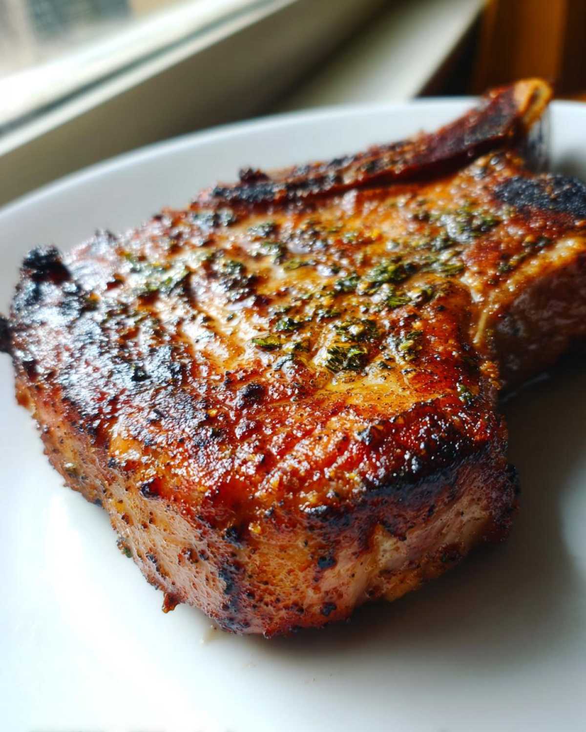 Close-up of a juicy, grilled pork chop showing a caramelized crust and herbs, prepared using the marinade for pork chops.