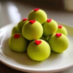 A stack of bright green, fuzzy Grinch Oreo Balls topped with small red candy hearts on a white plate.
