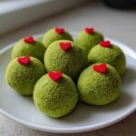 A plate of bright green, textured Grinch Oreo Balls topped with small red heart sprinkles.