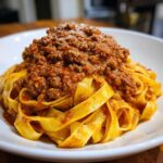 Close-up of rich bolognese sauce generously spooned over a bed of fresh tagliatelle pasta, topped with Parmesan.