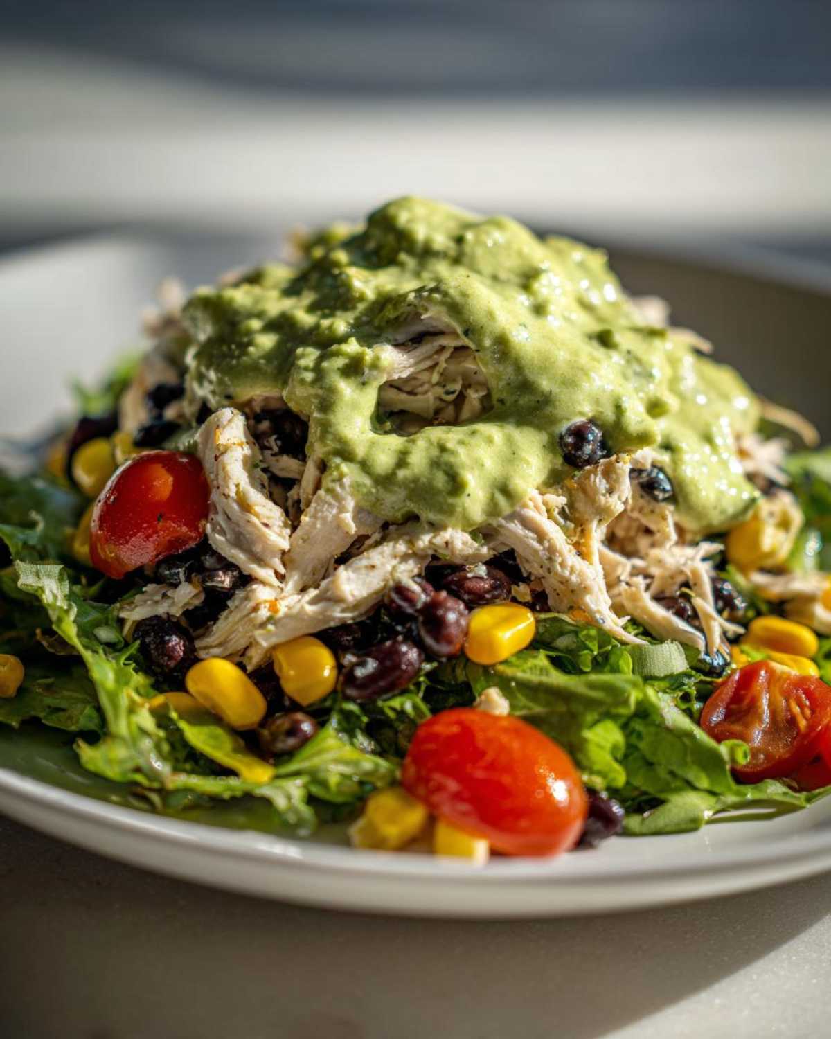 Close-up of a vibrant southwest chicken salad featuring shredded chicken, black beans, corn, tomatoes, and creamy green dressing.