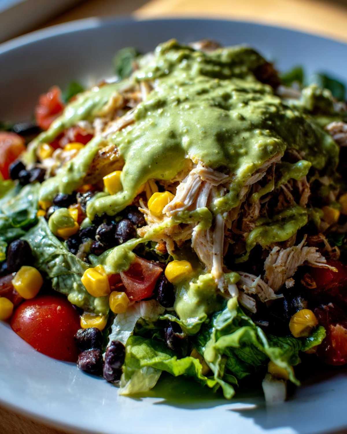 Close-up of a vibrant southwest chicken salad featuring shredded chicken, black beans, corn, tomatoes, and a creamy green avocado dressing.