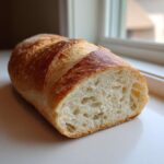 Close-up of a freshly baked french bread loaf cut in half, showing the airy interior crumb and golden crust.