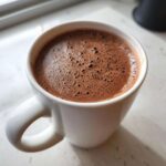 Close-up of rich, foamy homemade hot cocoa served in a white ceramic mug.