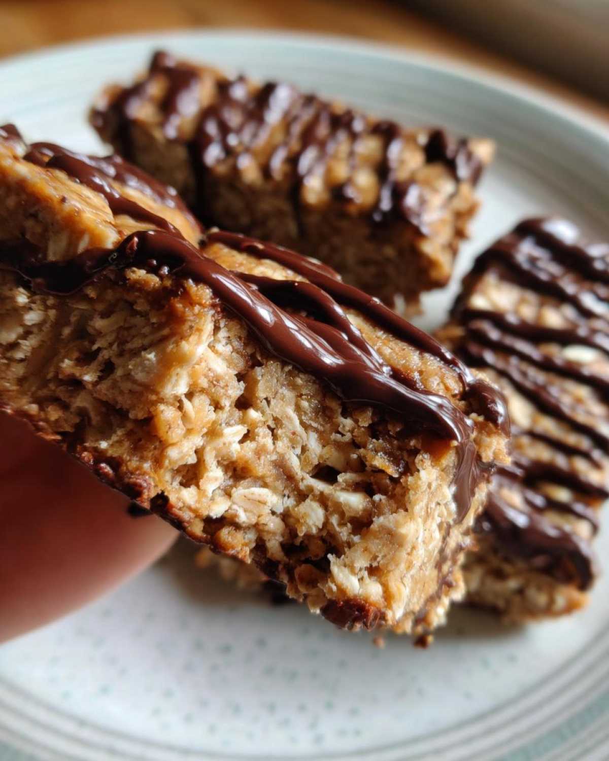 Close-up of a hand holding a textured, homemade protein bar drizzled with melted chocolate.
