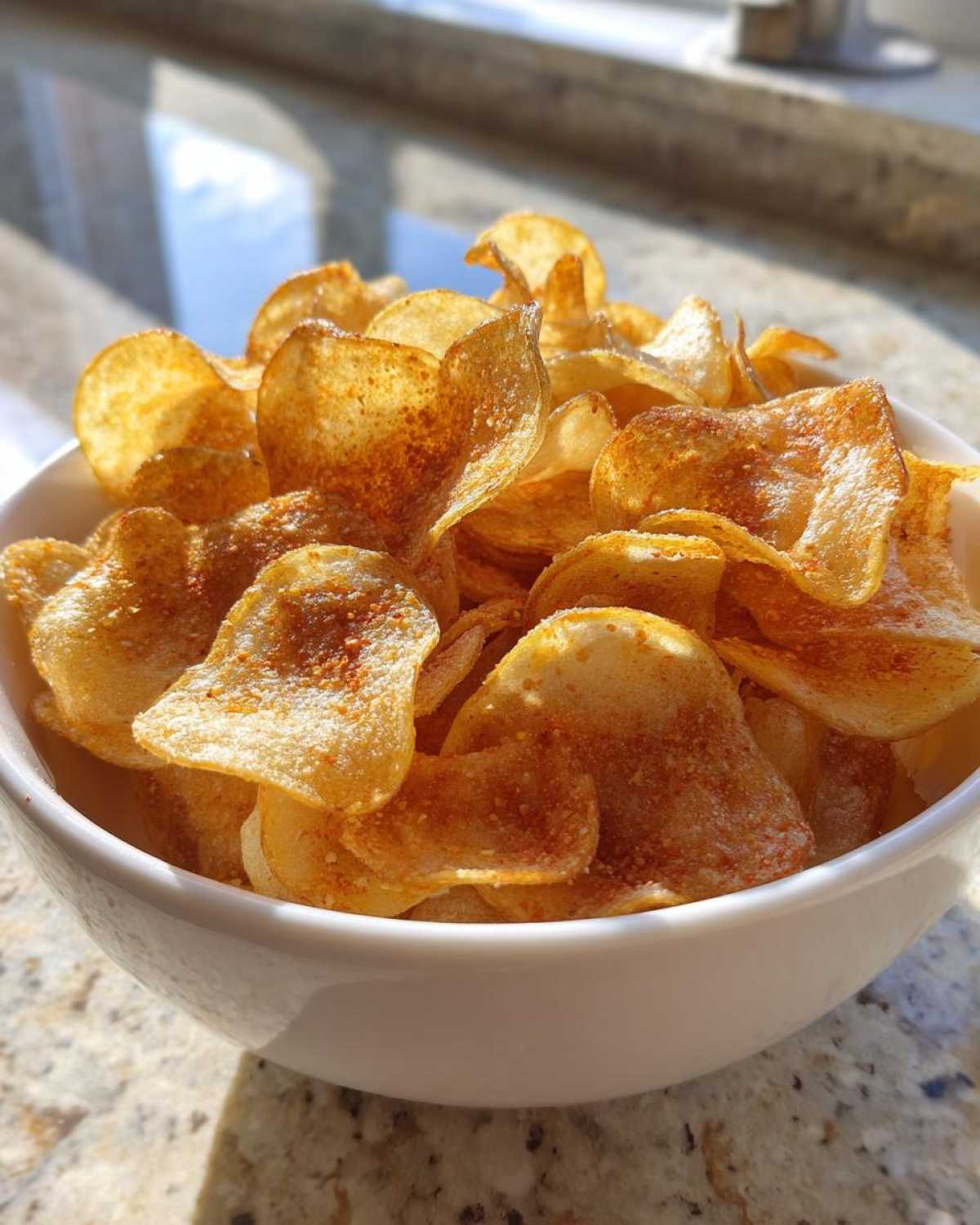 Close-up of a white bowl filled with crispy, golden homemade potato chips seasoned with spices.